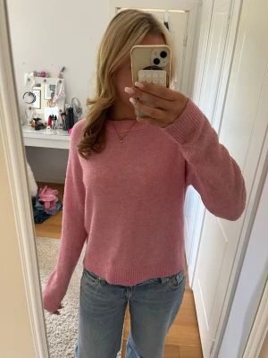 Rosa stickad tröja med rund hals - Mysig rosa stickad tröja med rund halsringning och långa ärmar. Tröjan har en enkel, klassisk design med ribbstickade muddar vid ärmslut och nederkant. Perfekt att matcha med jeans för en avslappnad look.
