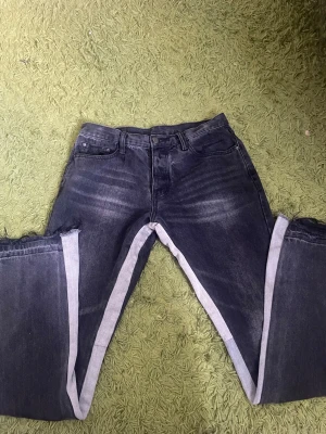 Mnmi flared jeans svarta - Unika svarta jeans med avklippta ben och råa kanter. Jeansen har klassisk femficksdesign och en tvättad look med ljusare partier framtill. Sidosömmarna är synliga längs benen för en edgy stil. Perfekta för dig som vill sticka ut. 30/32