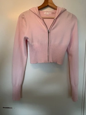 Ljusrosa cropped hoodie med dragkedja - Säljer en ljusrosa stickad hoodie med dragkedja framtill. Den är en kortare modell av stickad hoodie, i storleken 158/164