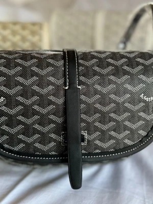 Svart axelväska från G0 - Snygg svart axelväska med det klassiska mönstret i vitt och grått. Väskan har rundad form, justerbar axelrem och detaljer i svart läder. Perfekt för dig som vill ha en unik och trendig accessoar.