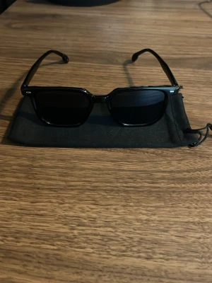 Raybandliknande solglasögon  - Snygga svarta solglasögon med rektangulära bågar och mörka glas. Klassisk och stilren design som passar till de flesta outfits. Kommer med en svart tygpåse för förvaring.det ska vara uv skydd men har inte testat för uv skydd