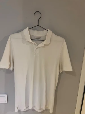 Vit pikétröja från Dressmann - Klassisk vit pikétröja från Dressmann med krage och korta ärmar. Tillverkad i bomull för en skön och luftig känsla. Perfekt till jeans eller shorts för en clean och enkel stil.