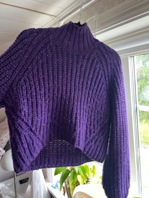 Lila stickad polotröja - Mysig lila stickad tröja med polokrage och ribbad struktur. Tröjan har lång ärm och en något croppad passform med snyggt mönsterstickat parti framtill. Perfekt för att hålla värmen under kyliga dagar.