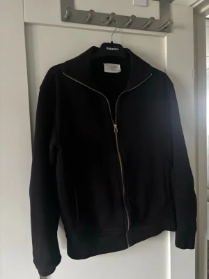 Svart ziptröja från Zara - Svart ziptröja från Zara Origins med hög krage och hel dragkedja framtill. Tröjan har långa ärmar, ribbade muddar och två sidofickor. Tillverkad i ett mjukt och bekvämt material som ger en clean och stilren look.