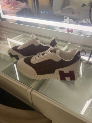 Skor - Snygga sneakers i vitt och vinrött med grov sula och en stor H-detalj på sidan. Ovandelen är i mesh-liknande material och har vita snören samt detaljer i mockaimitation. Perfekta för dig som vill sticka ut med en unik och trendig look.