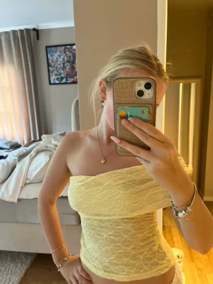 Gul spetsig offshoulder tubtopp - Snygg ljusgul tubtopp i spets med offshoulder-design. Toppen är croppad och har en figurnära passform som framhäver axlarna. Perfekt för dig som vill sticka ut med en feminin och trendig look. Minns ej vart den är ifrån har bara legat i garderoben!