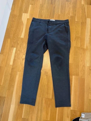 Mörkgrå kostymbyxor chinos tygbyxor medium - Snygga mörkgrå kostymbyxor från Perform Collection med slim fit passform. Byxorna har bälteshällor, knapp och dragkedja framtill samt sidfickor. Perfekta för en stilren look. Materialet känns mjukt och stretchigt. Mörkgrå stretch chinos byxor storlek 32x32 Sommarbyxor Midja 45 cm Längd 102 cm