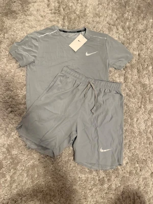 Nike -  Säljer ett helt nytt Nike miller dress ljusgrå färg. Setet består av en t-shirt och shorts.