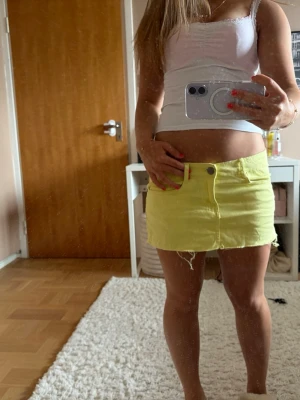 Gul jeanskjol  - Snygg gul minikjol i jeansmaterial med rå, fransig kant nertill. Kjolen har klassisk femficksmodell, knapp och dragkedja framtill samt bälteshällor. Perfekt för dig som vill sticka ut med färg i din outfit!