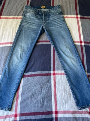 Blå slim fit jeans - Säljer ett par blå slim fit jeans från Jack&Jones i modellen GLENN. De är använda ett fåtal gånger och är i mycket bra/nytt skick. De säljs för att dom är för små. Jeansen har en snygg ljus tvätt med passformen slim fit. Perfekts för en trendig och avslappnad stil. 