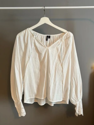 Vit blus med spetsdetaljer - Luftig vit blus med v-ringning och långa ärmar. Ärmsluten har fina spetsdetaljer och blusen har en avslappnad passform. Köpt på vero Moda i XS, aldrig använt💕