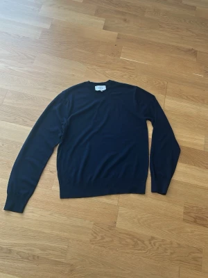 Mörkblå norvie ull tröja - 100% ull. En stilren mörkblå stickad tröja med rund halsringning och långa ärmar. Tröjan har en enkel design utan synliga mönster och ribbade muddar vid ärmslut och nederkant. Perfekt för lager på lager och passar till det mesta.