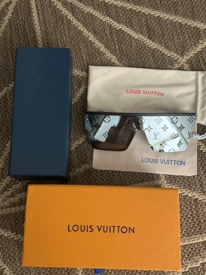 Louis Vuitton monogram solglasögon - Säljer ett par riktigt snygga Louis Vuitton solglasögon med spegelglas och ikoniskt monogrammönster över hela linsen. Sköldformad design med svart båge och silverfärgade detaljer. Kommer med originalfodral och förvaringspåse.