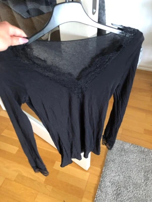 Intimissimi topp med spets  - Snygg svart långärmad topp med v-ringning och spetsdetaljer runt halsringningen och vid ärmsluten. Tunn och mjuk, perfekt att styla till olika looks. Figurnära passform och enkel att matcha med både jeans och kjol.