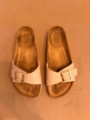 Beige slip-in sandaler med spänne - Snygga slip-in sandaler i beige med bred rem i skinnimitation och guldfärgat spänne. 