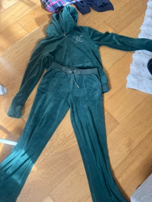 Grön sammetsloungewear Juicy Couture - Mysig mörkgrön loungewear-set från Juicy Couture i mjuk sammet. Setet består av en hoodie med dragkedja och fickor samt matchande byxor med snörning i midjan. Perfekt för chill dagar hemma eller när du vill vara extra comfy. Kan säljas bara byxor eller bara tröja med då priset diskuteras!