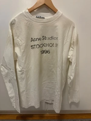 Vit långärmad t-shirt Acne Studios - Säljer en vit långärmad t-shirt från Acne Studios med tryck 'STOCKHOLM 1996' på bröstet. Klassisk rund hals och relaxed fit. Perfekt till jeans eller shorts för en clean och stilren look.