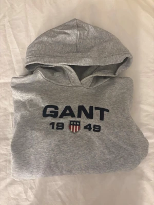 Grå oversizedhoodie/ hoodieklänning från GANT - Mysig grå hoodieklänning från GANT med broderad logga och texten '1949' framtill. Långärmad modell med huva och ribbade muddar. Perfekt för chill dagar hemma eller som loungewear. Tillverkad i mjukt sweatshirtmaterial. Hoodien är i storlek 158/164💕