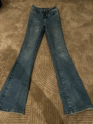Blå Peachy flare jeans med utsvängda ben - Säljer ett par klassiska blå Peachy flare jeans. Jeansen har normalhög midja och är gjorda i denim med lätt tvättade detaljer. WAIST XS LENGTH 33