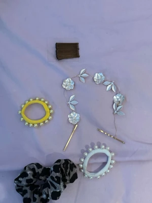 Mix av håraccessoarer med pärlor - Säljer ett kit med håraccessoarer: två hårsnoddar med pärlor (en gul och en vit), ett svart scrunchie med leopardmönster, ett set bruna hårnålar och ett dekorativt hårband med vita blommor och blad. Perfekt för att piffa till frisyren med olika stilar.
