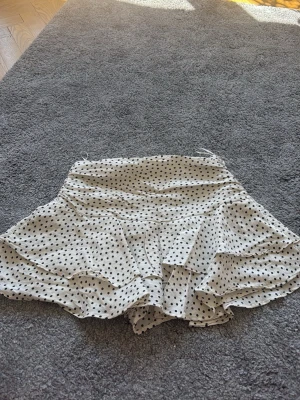 Vit prickig kjol från ZARA - Superfin vit kjol från ZARA med svarta prickar och volangig nederdel. Kjolen har inbyggda shorts i sig. Använd en gång och säljer då den är för liten.