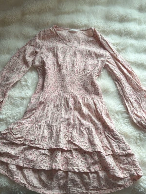 Blommig rosa klänning från H&M - Söt rosa klänning från H&M med små blommor, v-ringning och långa ärmar. Klänningen har smock i midjan och volangdetaljer på kjolen. Perfekt för vår och sommar med sitt lätta bomullsmaterial. Finns djur i hemmet, tvättas såklart innan skickning. Går även super att fråga om vi kan stryka den🥰 har använt denna på en skolavslutning+ misommar💕 