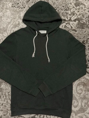 Mörkgrön hoodie med vita snören - Snygg mörkgrön hoodie från PIER ONE med klassisk huva och vita dragsnören. Hoodien har en enkel design, ribbade muddar vid ärmslut och nederkant samt en stor magficka framtill. Perfekt för en avslappnad och stilren look.