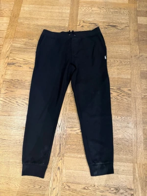 Svarta Ralph Lauren mjukisbyxor med dragsko - Säljer ett par svarta mjukisbyxor med dragsko i midjan och muddar vid bensluten. Byxorna har en liten broderad logga på vänster sida och fickor fram. Perfekta för chill dagar eller när du vill vara bekväm.