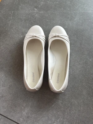 Vita ballerinaskor från Graceland - Snygga vita ballerinaskor från Graceland med rund tå och dekorativ rosett framtill. Skorna har en enkel och stilren design i ett slätt material som ger en fräsch look. Perfekta för dig som gillar klassiska och tidlösa skor.