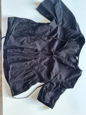 Svart blus från Divided H&M - Snygg svart blus från Divided H&M i storlek XS. Blusen har trekvartsärm, knytband i midjan och en lätt rynkad nederdel. Tillverkad i ett tunt och mjukt tyg som ger en avslappnad men trendig look.