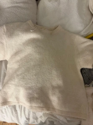 Krämvit stickad tröja Gina Tricot - Mysig krämvit stickad tröja från Gina Tricot med enkel design och rund halsringning. Tröjan har långa ärmar och ribbstickade muddar vid halsen. Perfekt för lager på lager under kyliga dagar.