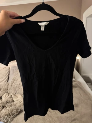 Svart t-shirt med v-ringning - En enkel svart t-shirt med v-ringad hals och korta ärmar. Perfekt basplagg som passar till det mesta. Tillverkad i mjukt material för skön känsla och avslappnad passform.