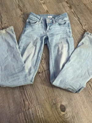 Ljusblå raka jeans från Nelly - Säljer ett par ljusblå jeans från Nelly med raka ben och snygga broderade detaljer i rosa på bakfickorna. Jeansen har klassisk femficksdesign och bälteshällor. Perfekta för en avslappnad och trendig look.