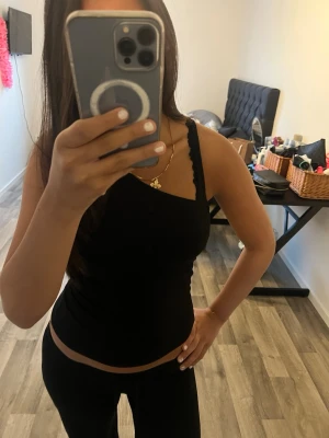 Svart oneshoulder topp - Snygg svart oneshoulder topp med smal axelrem och figurnära passform. Toppen är ärmlös och har en stilren, enkel design som passar perfekt till jeans eller kjol. Perfekt för dig som gillar en trendig och minimalistisk look.
