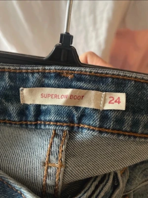 Blå superlow bootcut jeans - Säljer ett par blå jeans med superlow midja och bootcut-modell. Jeansen har klassisk femficksdesign, ljus tvätt och kontrastsömmar. Perfekta för dig som gillar en avslappnad men ändå trendig look.