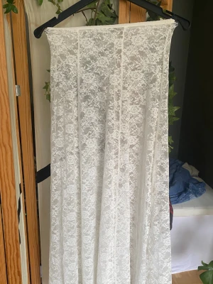 Vit lång spetskjol från Kappahl - Säljer en vit långkjol från Kappahl i genomskinlig spets med blommigt mönster. Kjolen har en rak och flowy passform och är perfekt för sommaren. Resår i midjan för extra komfort. Använd kanske en gång, utmärkt skick!