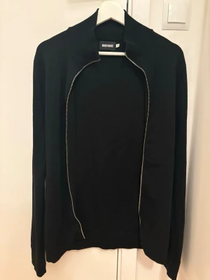Merino Hel Zip - Snygg svart zip-up tröja i skön merino ull från Brothers. Klassisk modell med hög ribbad krage, hel dragkedja och ribbade kanter. Perfekt som mellanlager eller ensam plagg. Storlek: M Material: 100% Merino ull Skick: Bra skick med en liten defekt vid axeln (se bild), men den syns inte när man har tröjan på sig. Priset är inte hugget i sten så vid snabb affär kan det justeras.  Original pris 1499kr