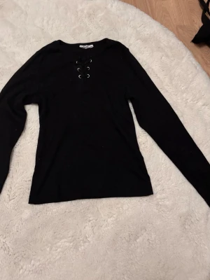 ribbad topp med snörning - Långärmad topp med ribbad struktur och snygg snörning framtill vid halsen. Perfekt för dig som gillar en enkel men ändå trendig stil. Passar till både jeans och kjol för en cool vardagslook.