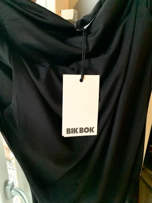 Svart asymmetrisk meshtopp - Svart, asymmetrisk topp med lager av mesh utanpå och med långa volanger nedtill. Kan bäras på olika sätt - se bilder. Endast provad. Stilren design som ändå sticker ut!