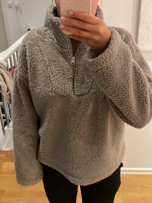 Beige teddyjacka från BikBok - Mysig grå teddyjacka från BikBok i återvunnet material. Jackan har halv dragkedja framtill, hög krage och en oversized passform som ger en avslappnad look. Perfekt för kalla dagar när du vill vara både varm och trendig.