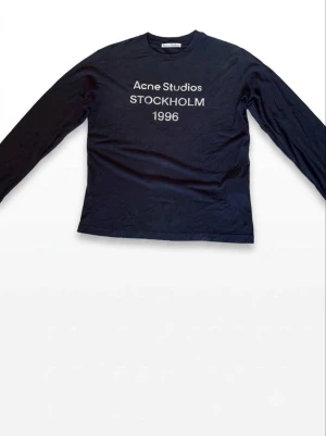Svart långärmad topp Acne Studios - Svart långärmad topp från Acne Studios med tryck 'Acne Studios STOCKHOLM 1996' på bröstet. Klassisk rund halsringning och rak passform. Perfekt till jeans eller kjol för en clean look