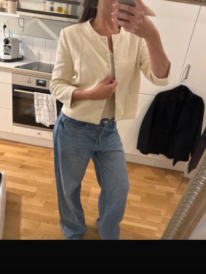 Krämvit kavaj från Mango Suit - Stilren krämvit kavaj från Mango Suit med rund halsringning och knäppning framtill. Kortare modell som ger en modern look. Tillverkad i ett lätt tyg som passar perfekt till jeans eller kjol. Enkel och snygg design utan krage.                                    Lånade bilder då den är för liten, skriv så kan jag skicka andra bilder på den.