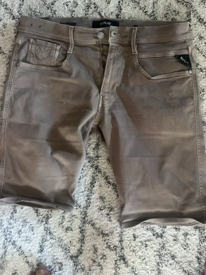 Bruna shorts från Replay - Snygga bruna shorts från Replay med klassisk femficksdesign och knappgylf. Shortsen har en rak passform och är tillverkade i ett mjukt bomullsmaterial som känns skönt mot huden. Perfekta för varma dagar och enkel att matcha med olika stilar.