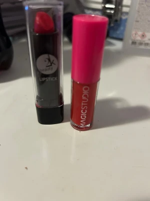 Rött läppstift & läppglans Magic Studio - Säljer ett rött läppstift i klassisk hylsa samt ett flytande rött läppglans från Magic Studio med rosa lock. Båda produkterna har en röd färg och är perfekta för att skapa en snygg look. Läppstiftet har genomskinligt lock och svart botten.