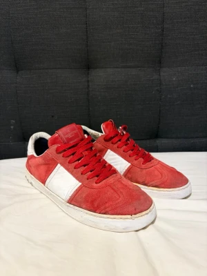 Valentino flycrew  - Snygga röda sneakers från Valentino med vita detaljer på sidan och vit sula. Skorna har röd mocka, röda skosnören och en klassisk låg siluett. Perfekta för dig som vill sticka ut med stilrena och trendiga skor.