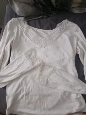 Vit långärmad topp med spetsdetaljer - Har en super liten fläck🥰 Snygg vit långärmad topp med v-ringning och fina spetsdetaljer vid halsringning och ärmslut. Perfekt för dig som gillar en romantisk och feminin stil. Mjuk och bekväm, passar till många olika outfits.