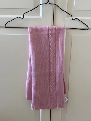 Rosa stickad halsduk från Adidas - Säljer en mjuk och snygg rosa stickad halsduk från Adidas. Halsduken har ett diskret flätmönster längs ena sidan och en liten metallbricka med Adidas-loggan. Använd en gång. 