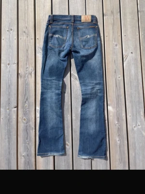 Blå bootcut jeans med kontrastsömmar - Säljer ett par klassiska blå bootcut jeans med snygga kontrastsömmar och broderade bakfickor. Jeansen har normalhög midja och en patch i läderimitation bak i linningen. Perfekta till sneakers eller boots för en avslappnad look.