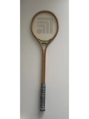 Badmintonracket Fukuda aluminium - Säljer ett badmintonracket från Fukuda i högtempererad aluminiumlegering. Racketen är guldfärgad med svart och grått handtag och har ett klassiskt rutnät av strängar. Perfekt för dig som gillar att spela badminton och vill ha ett stabilt racket.