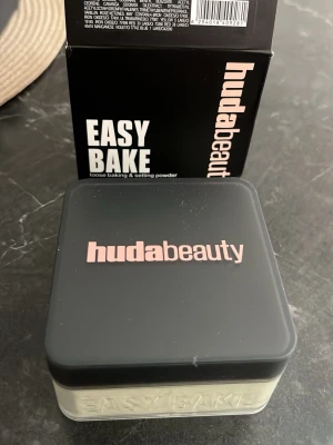 Huda Beauty Easy Bake löspuder - Löspuder från Huda Beauty i modellen Easy Bake. Kommer i en fyrkantig burk med svart lock och transparent underdel där pudret syns. Pudret är ljust beige och används för att fixera foundation och ge en matt finish.